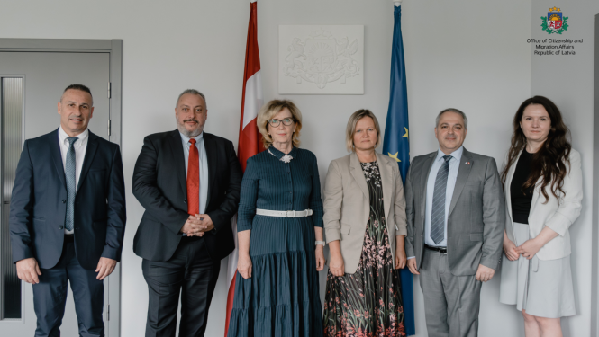 Representatives of the OCMA stand next to representatives of the Israeli delegation. In the background - the Latvian flag.