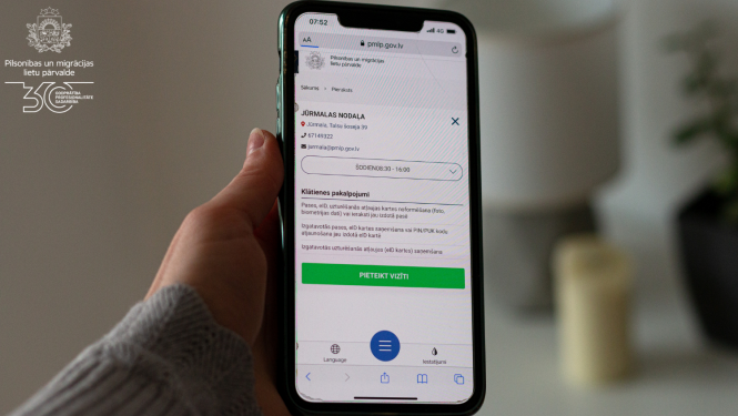 roka, kas tur mobilo telefonu ar atvērtu Qticket aplikāciju