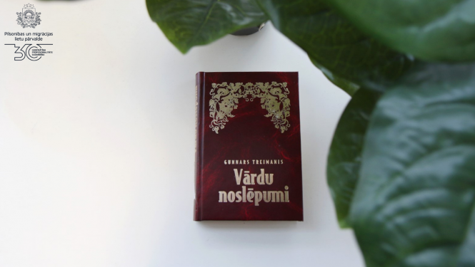 Grāmata uz galda "Vārdu noslēpumi" tumši sarkanajos vākos