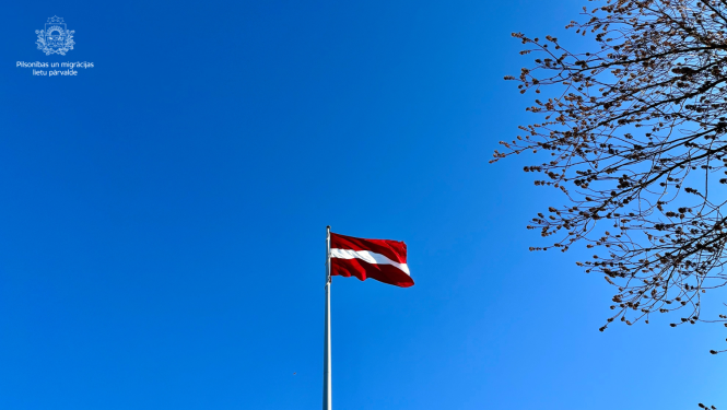 Latvijas karogs uz zilo debesu fona