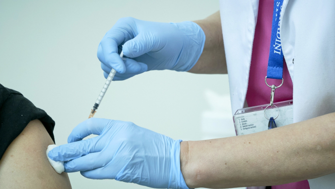 Ārsta rokas medicīniskajās cimdos taisa vakcīnu citam cilvēkam