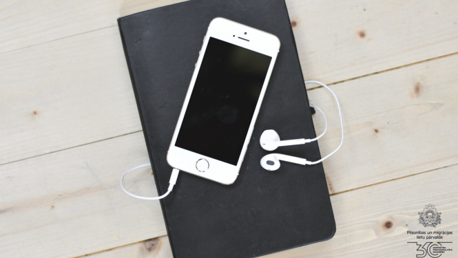 Uz galda: pierakstu klade melnajos vākos un mobilais tālrunis