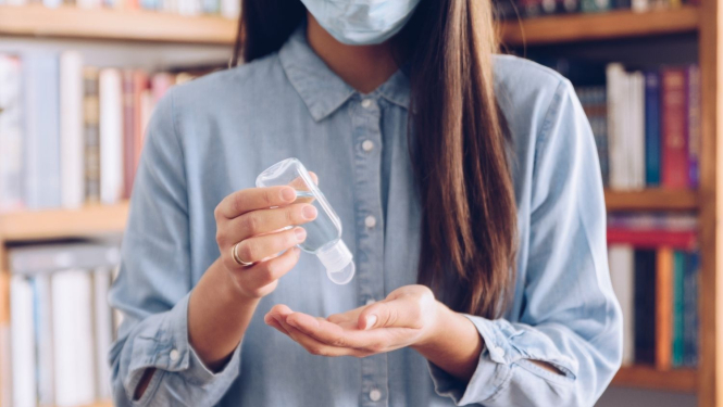 Sieviete ar gariem tumšiem matiem ar mutes un deguna aizsegu sejā dezinficē rokas