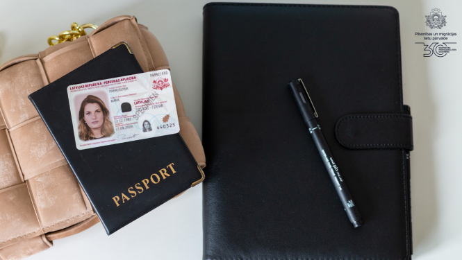 Uz galda: pierakstu klade melnajos vākos ar melnu pildspalvu, bēšīgās krāsas soma, un uz tās - pase melnajos vākos ar uzrakstu "Passport" un jaunā parauga ārzemnieku eID karte