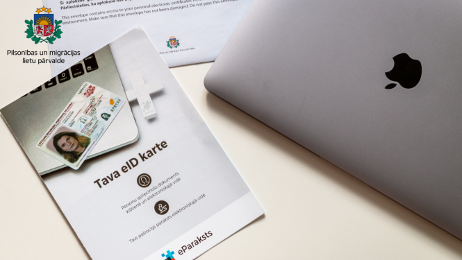 Uz galda stāv brošūra par eID karti, portatīvais dators