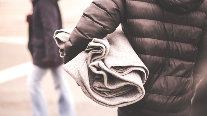 No mugurpuses nofotografēts cilvēks, kurš nes rokā saliktu segu