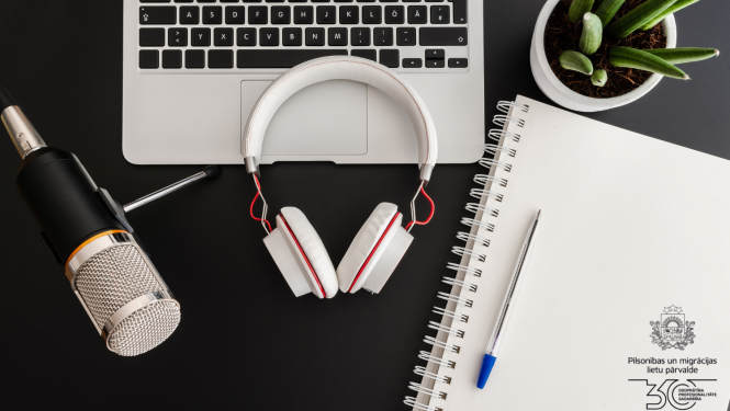 uz galda: austiņasmikrofons, portatīvais dators, pierakstu klade