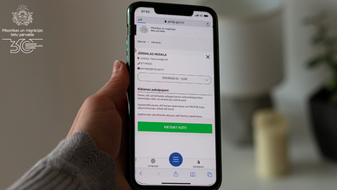 roka, kas tur mobilo telefonu ar atvērtu Qticket aplikāciju