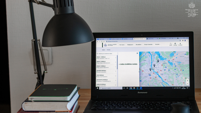 Uz galda stāv lampa un portatīvais dators ar atvērtu iepriekšējā pieraksta sistēmu