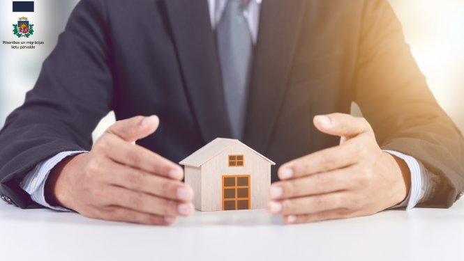 VĪRIEŠA ROKAS UN MAZA MĀJIŅA UZ GALDA