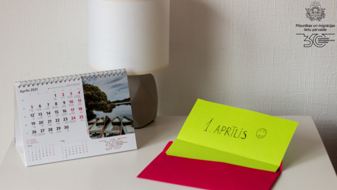 Kompoz'icija uz galda: galda kalendārs un līmlapiņā spilgti dzeltenā kr;as;a ar uzrakstu "1. aprīli :)"