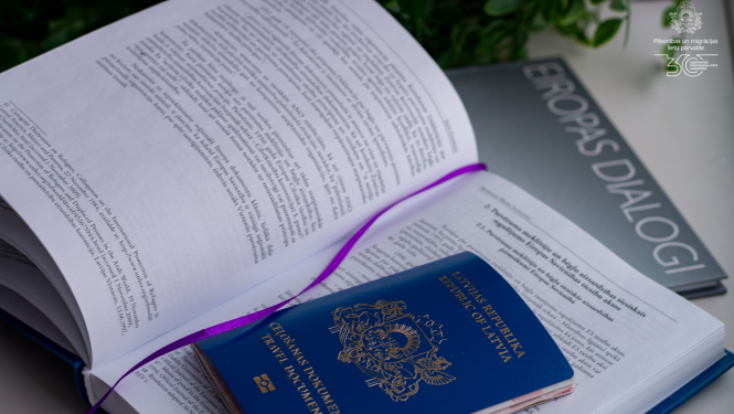 Atvērta grāmata, tajā ielikta zilā pase ar nosaukumu "Ceļošanas dokuments"