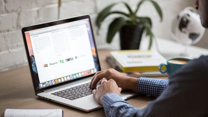 Uz galda stāv portatīvais dators, ir redzamas cilvēkas rokas, aizmugurēā plānā - istabas zieds podā