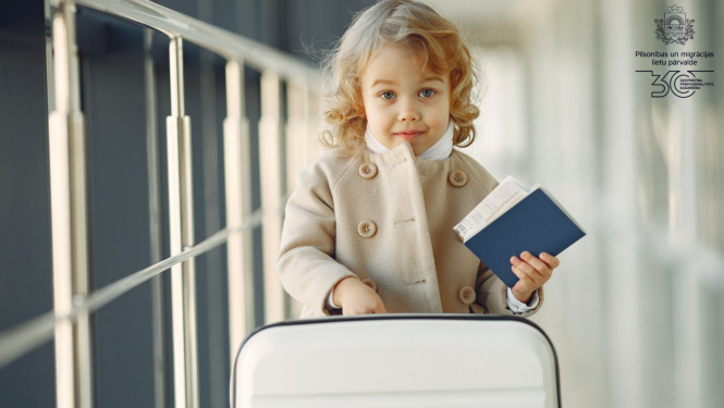 Mazs bērns stāv blakus koferim ar papīriem rokās