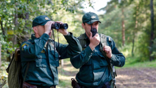Divi vīrieši robežsardzē. Viens runā rācijā, otrs skatās binoklī