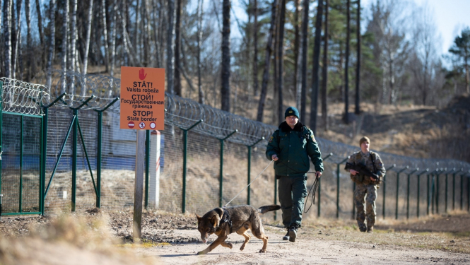 Divi robežsargi skrien gar robežu, viens ar suni, otram rokās - šaujamais ierocis