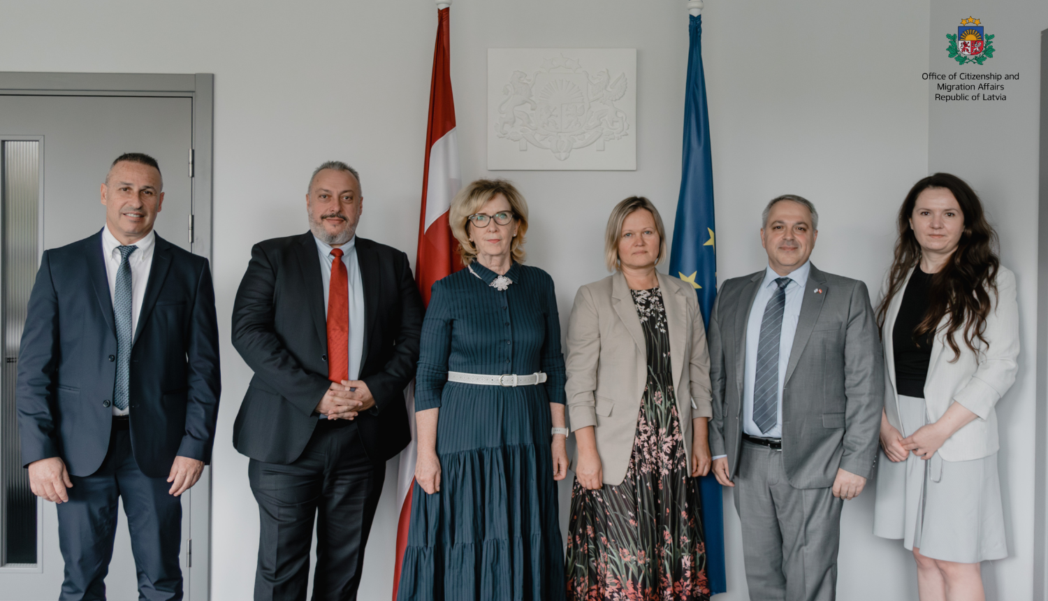 Representatives of the OCMA stand next to representatives of the Israeli delegation. In the background - the Latvian flag.