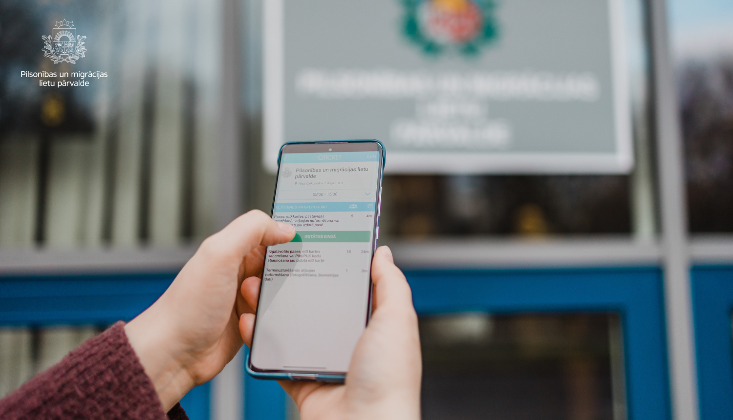 Cilvēka roka ar mobilo telefonu, kur ir "atvērta" Qticket mobila lietotne