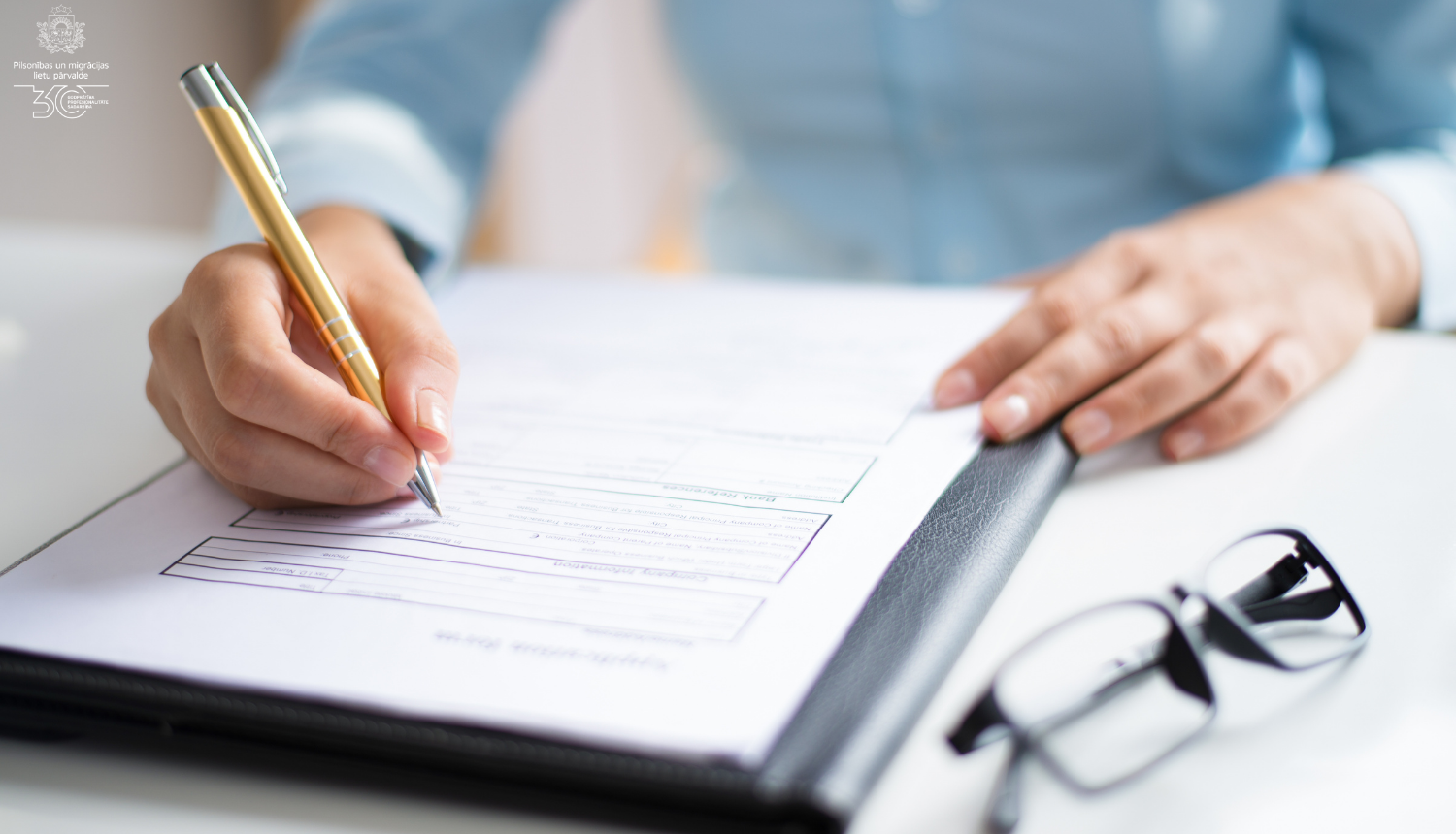 Cilvēka roka raksta uz papīra, blakus uz galda - brilles