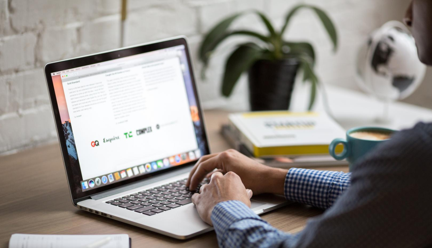 cilvēka rokas, sēžot aiz galda pie portatīva datora, skats no muguras