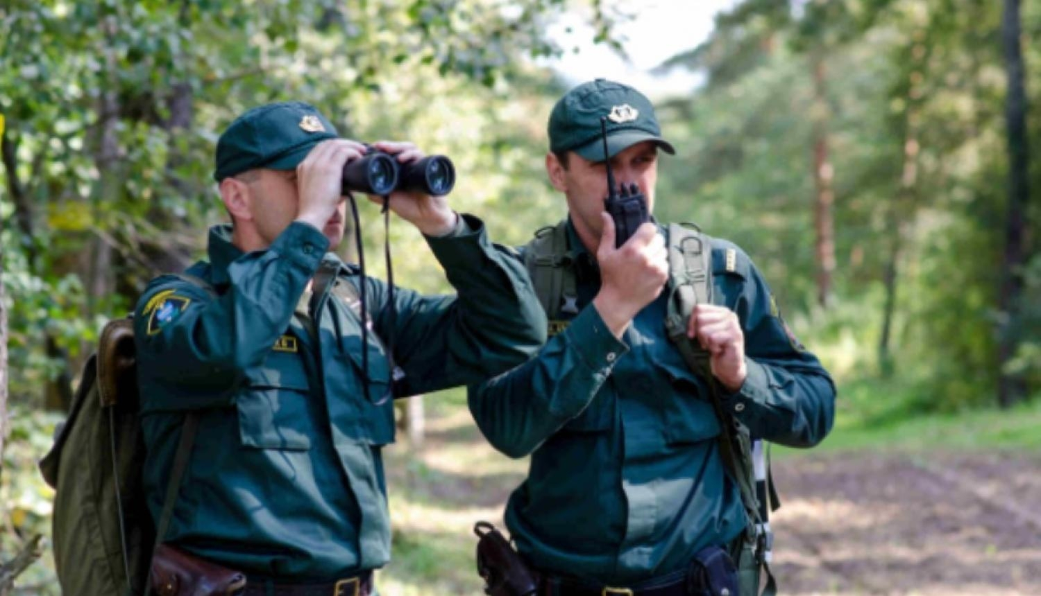 Divi vīrieši robežsardzē. Viens runā rācijā, otrs skatās binoklī