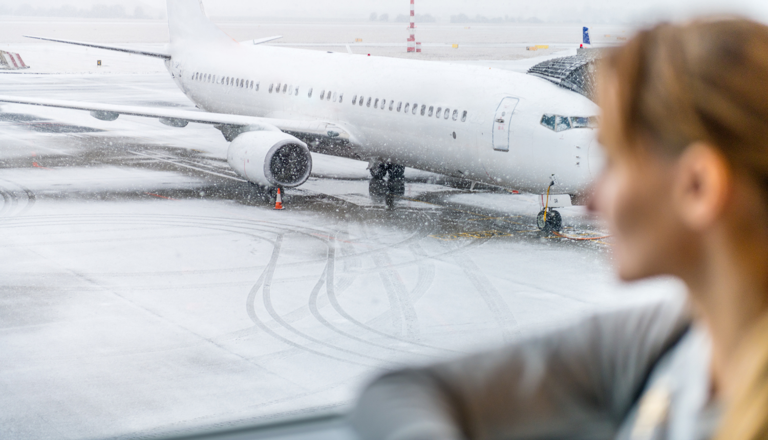 Sieviete, kura gaida pie lidmašīnas loga, vērojot pa logu lidmašīnu, kas gatavojas reisam