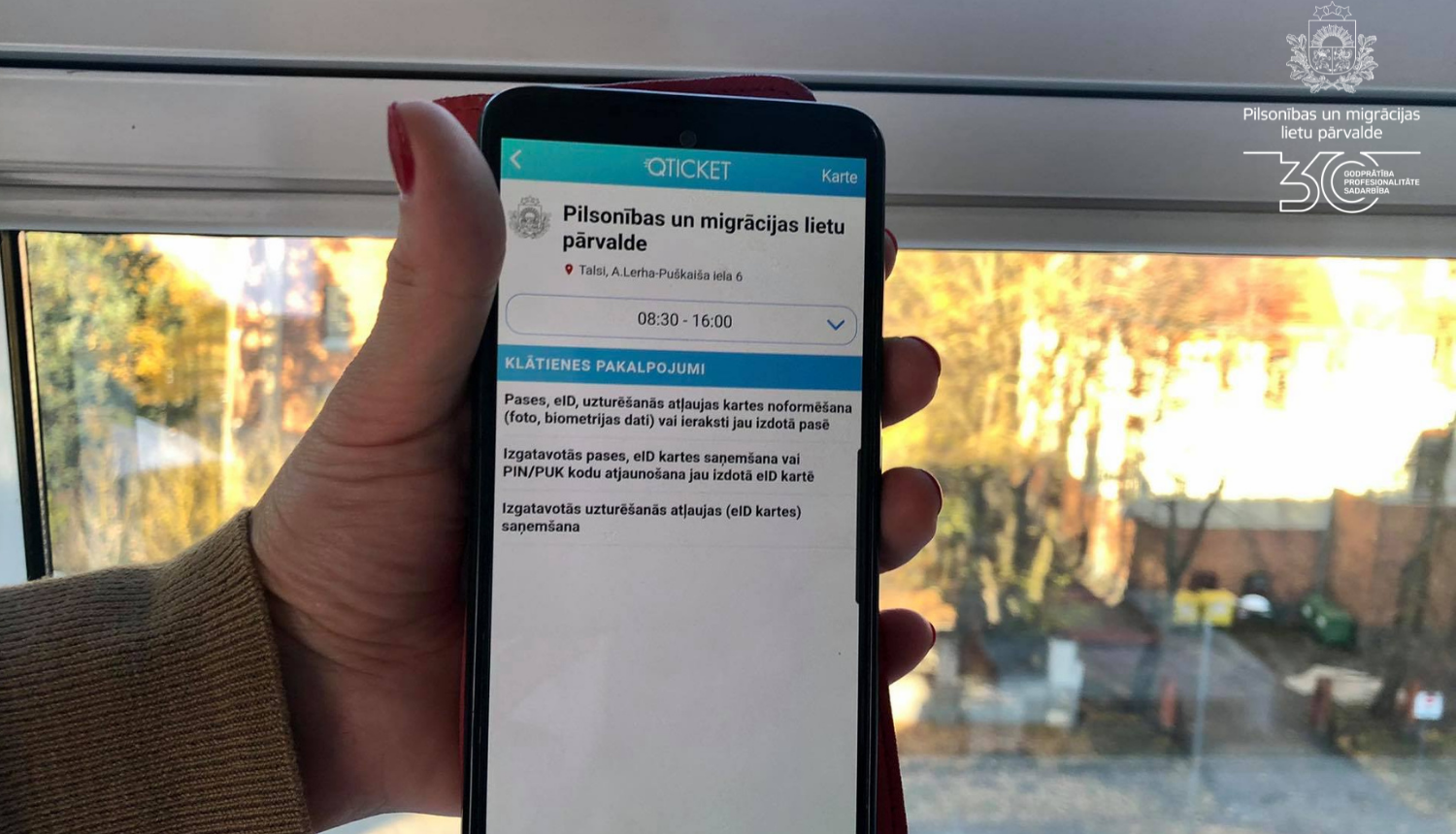 Mobilais telefons rokās ar atvērtu Qticket programmu un iespēju veikt pierakstu PMLP talsu nodaļā